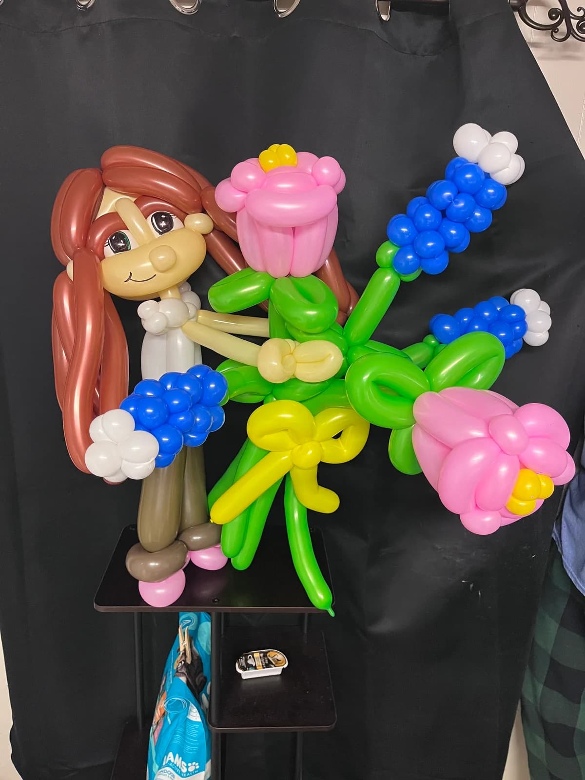 Balloon caricature with long brown hair beside a flower bouquet