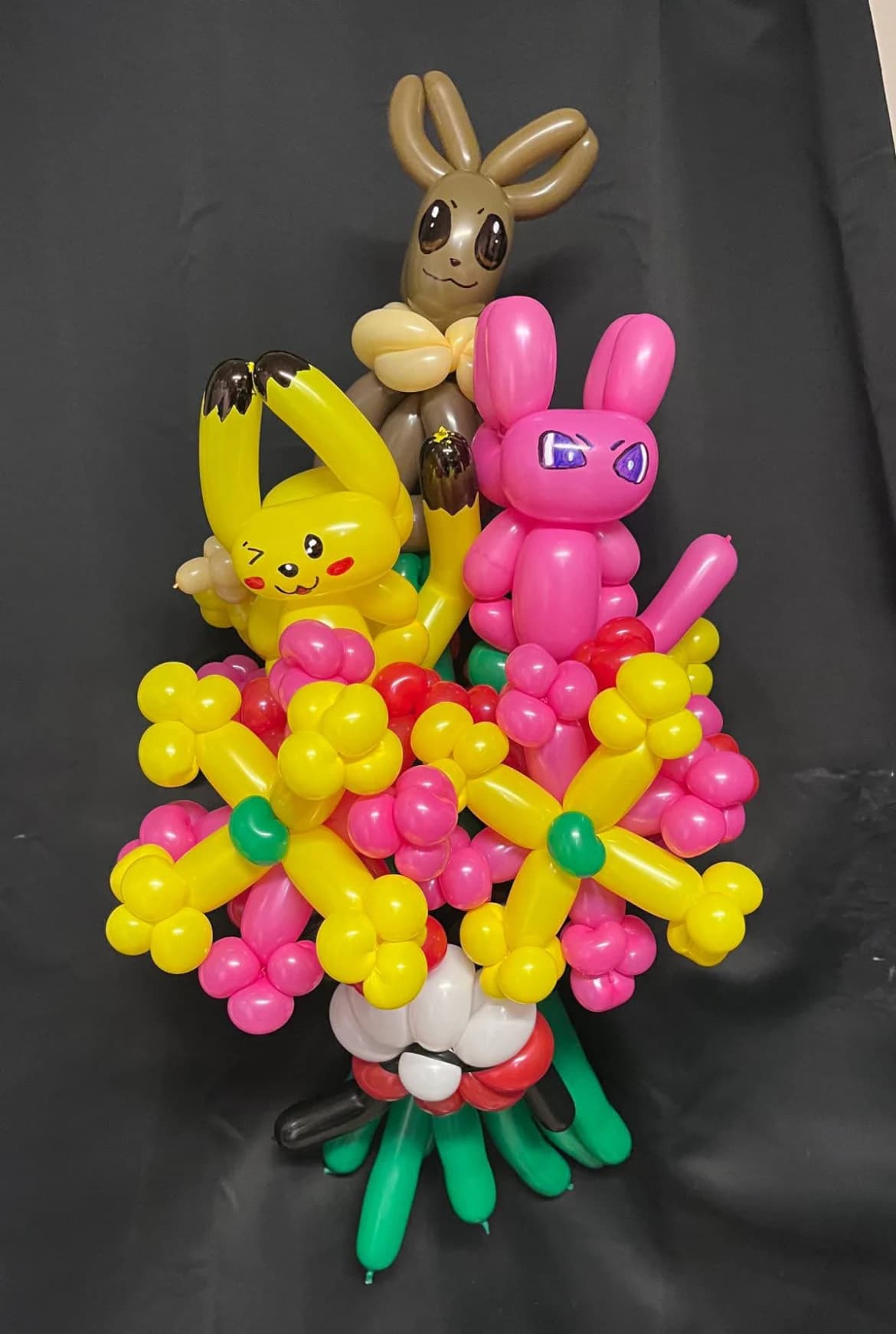 Three colorful balloon characters arranged above a flower bouquet